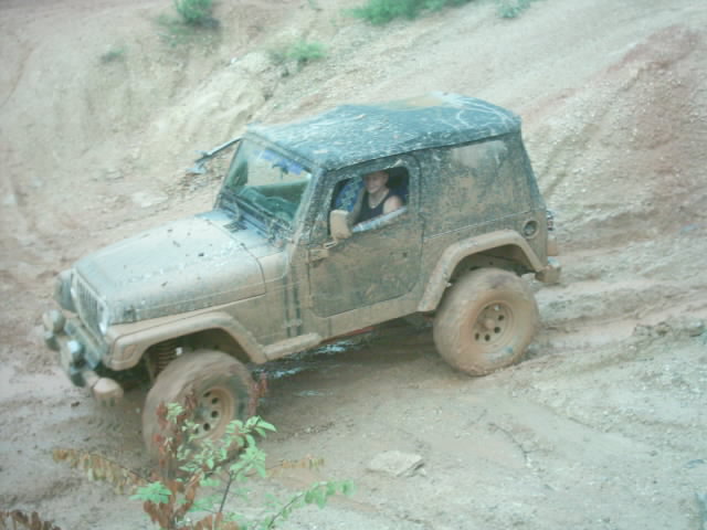Mud-covered 2003 Jeep Wrangler on a dirt trail, driver visible inside