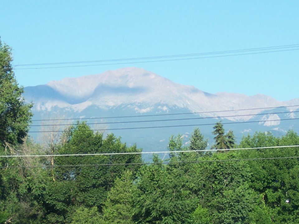 Mountain range under a clear blue sky, with green trees in the foreground