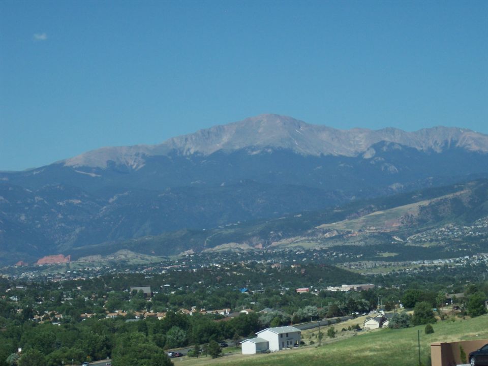 Mountain range overlooks a town and green hills under a clear blue sky