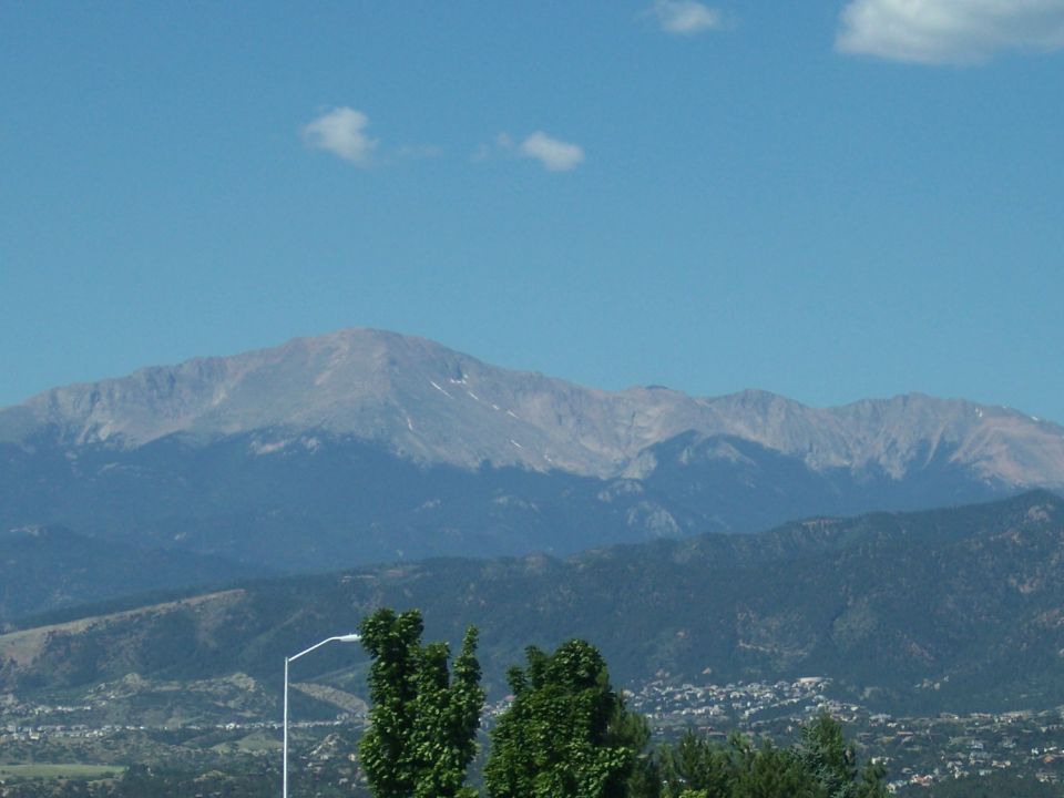 Mountain range under a blue sky with scattered clouds. Trees and a street light are in the foreground