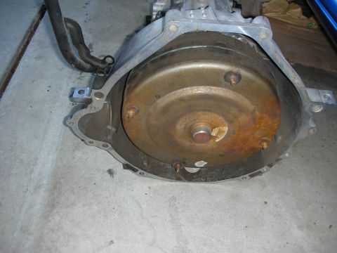 1998 Ford Crown Victoria - Close-up of a rusty torque converter and transmission bell housing assembly.