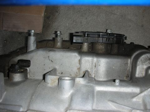 1998 Ford Crown Victoria - Close-up of a used cast-aluminum automatic transaxle or transmission case laid on a blue surface, showing bolt studs, a black plastic senso…
