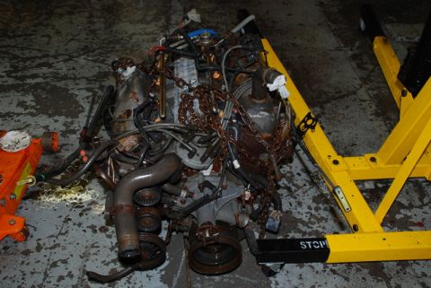 1996 Ford Bronco - A disassembled engine sits on a yellow engine stand in a garage, with an orange jack nearby.