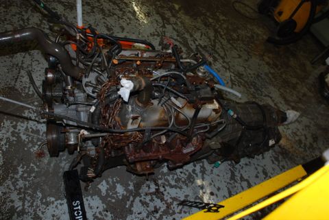 1996 Ford Bronco - A heavily rusted engine and transmission assembly lies on a stained concrete floor.