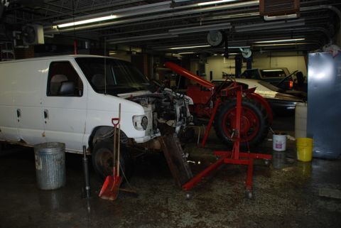 1996 Ford Bronco - A white van sits in a garage with its front end disassembled, next to a red tractor and a pickup truck.