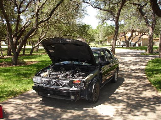Car with hood open, bumper removed, parked on a driveway