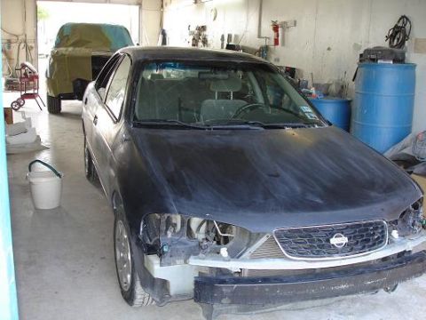 1996 Ford F-150 - A black sedan is in a garage, undergoing repairs with its front bumper and headlights removed. Another vehicle is covered in the background.