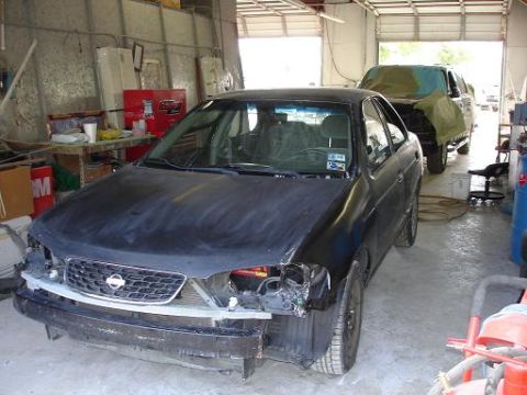 1996 Ford F-150 - Two vehicles are in a garage, one a Nissan sedan undergoing repairs, the other a covered truck.