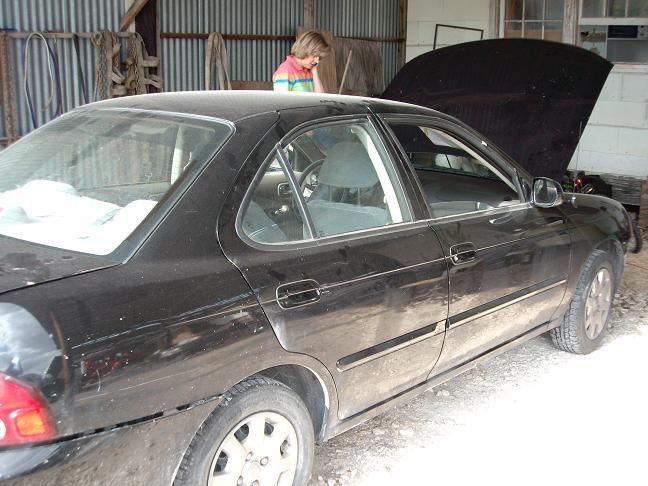 Black sedan with hood up in a garage. Person in background