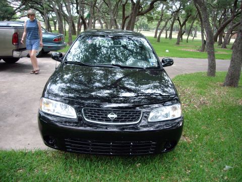 1996 Ford F-150 - A black sedan is parked outdoors with trees in the background. Another vehicle and a person are visible to the left.