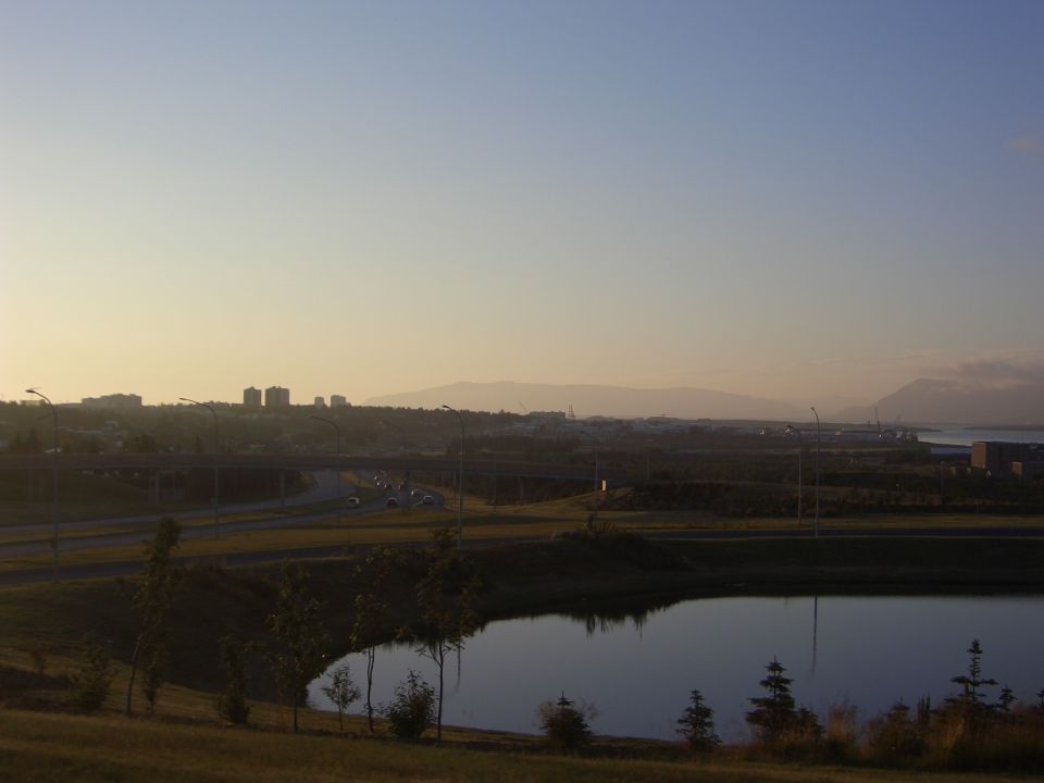 Landscape scene with a highway, distant city skyline, and a body of water at sunset