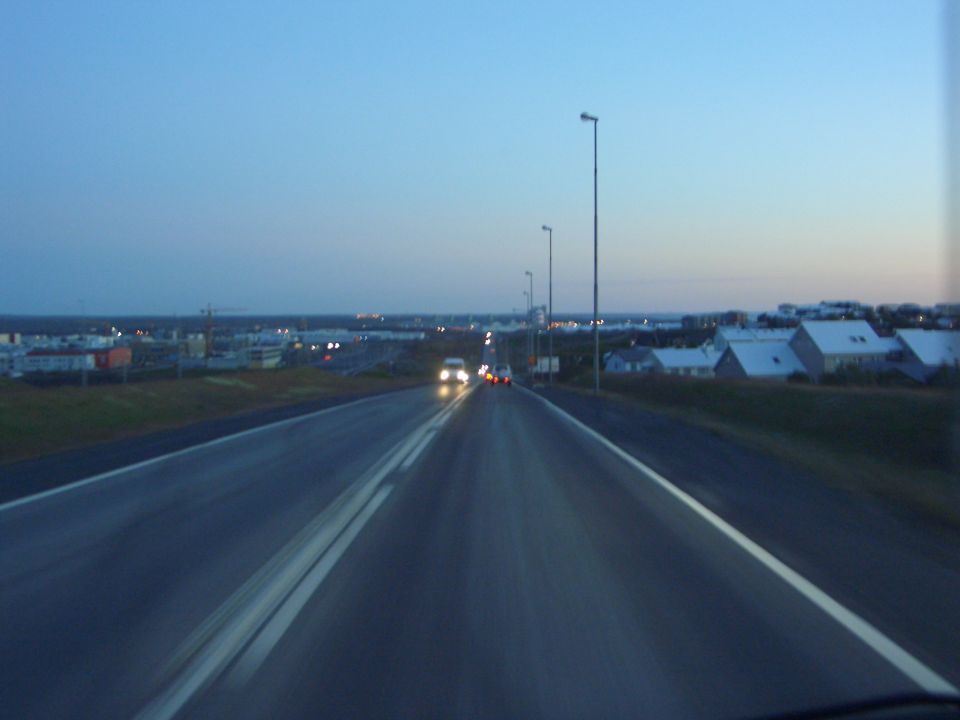 View from a moving vehicle on a highway approaching a town at dusk