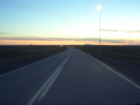 1974 Ford Bronco - A lonely road winds through a flat landscape under a twilight sky with distant lights.