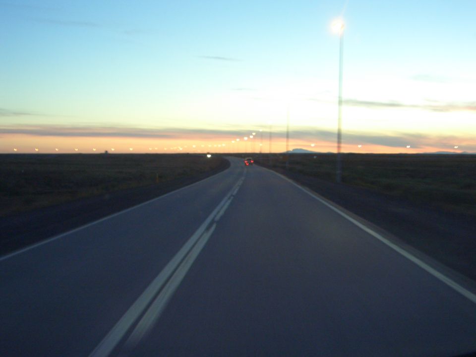 Road stretching into the distance at dusk with a single car visible far ahead