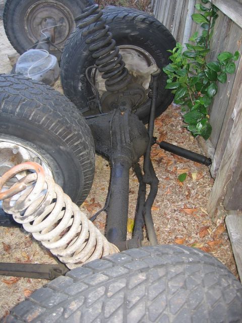 1989 Ford Bronco - Vehicle suspension components are visible, including tires, springs, and shocks, near a wooden fence.