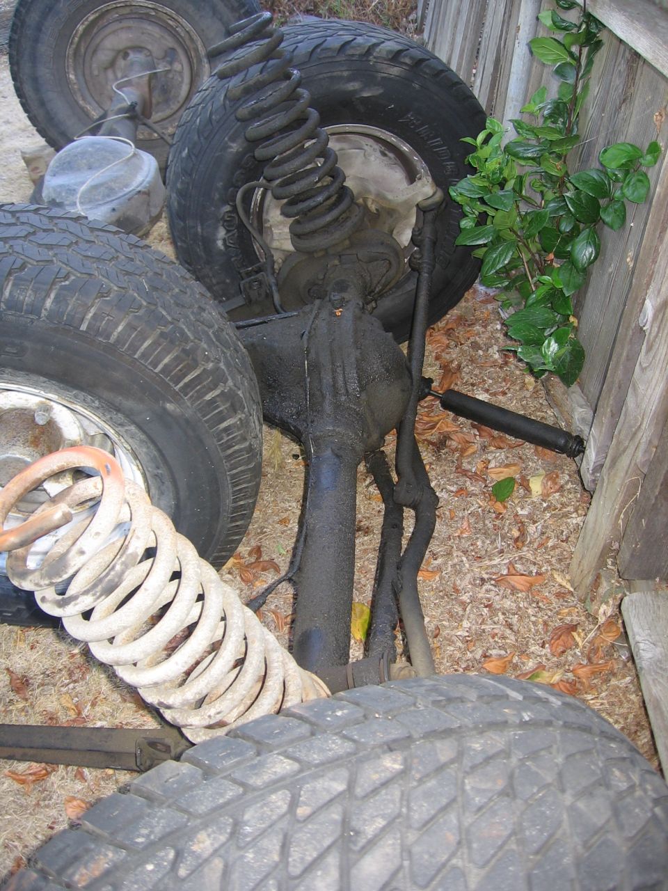 Vehicle suspension parts including shocks, springs, and tires piled near a wooden fence