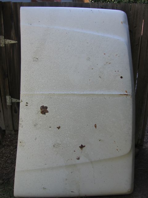 1989 Ford Bronco - A weathered white hood, likely from an older truck or SUV, rests against a rustic wooden fence, showing signs of age and exposure.