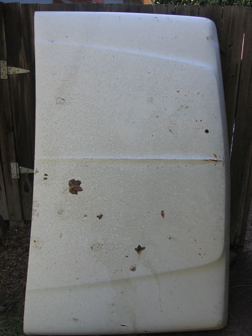 White hood with rust spots and leaves, leaning against a wooden fence