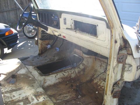 1989 Ford Bronco - The interior of a heavily rusted white truck cab shows significant wear and missing components.