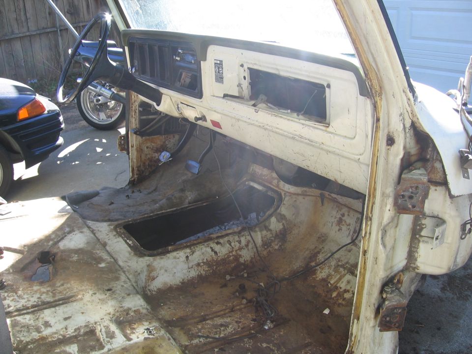 White truck cab interior, heavily rusted floor and dashboard, missing glove box and radio