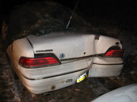 1992 Ford Crown Victoria - A white sedan shows severe damage to its rear bumper and trunk area, partially obscured by a dark tarp.