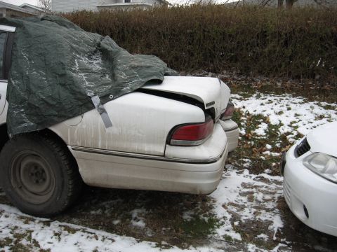 1992 Ford Crown Victoria - A white sedan with a tarp over its front half sits in the snow, showing damage to its trunk.