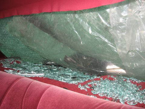 1992 Ford Crown Victoria - The interior of a 1992 Ford Crown Victoria shows a shattered rear window with glass fragments scattered across the red upholstery.