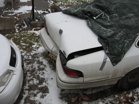 1992 Ford Crown Victoria - Rear view of a damaged 1992 Ford Crown Victoria, partially covered by a tarp, parked in snowy conditions.