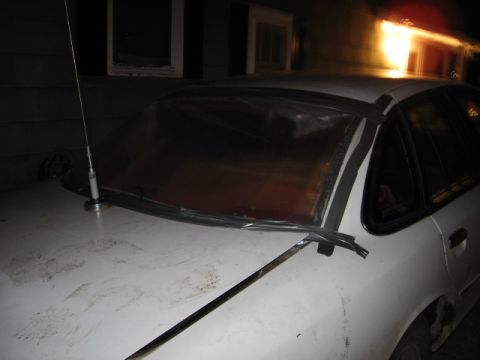 1992 Ford Crown Victoria - A white 1992 Ford Crown Victoria has its windshield covered with a tarp and tape, with a crowbar resting on the hood.