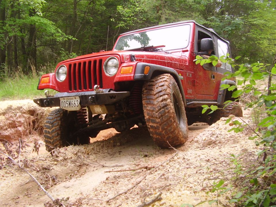 Red 2003 Jeep Wrangler on a dirt trail, front-left tire angled up