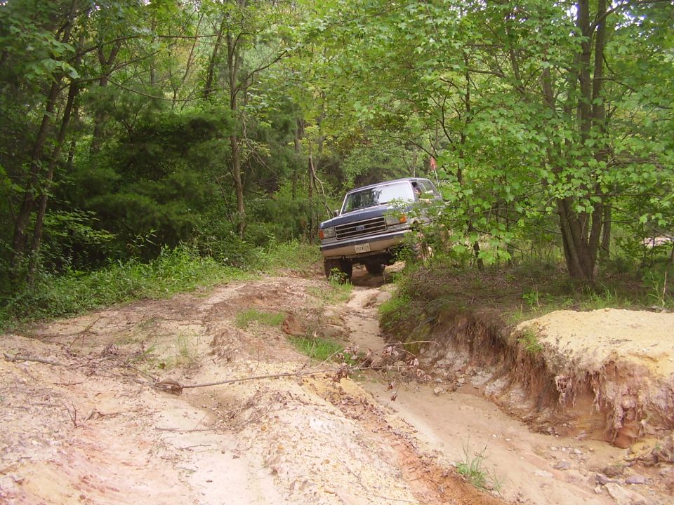 Blue Ford Bronco driving on a dirt trail through woods
