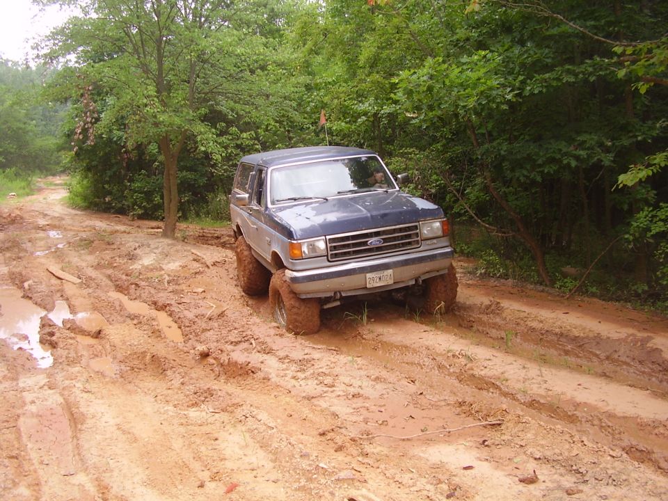 Blue and silver Ford Bronco navigating a muddy path, tires caked in mud
