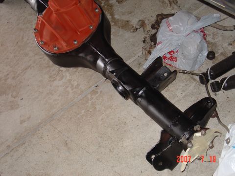 1973 Ford Ranchero - A black rear axle assembly with an orange differential cover sits on a concrete surface, with a plastic bag and other parts in the backgrou…