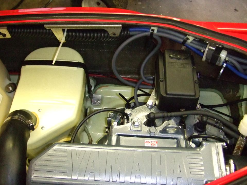 Engine bay with a cast Yamaha valve cover, plug wires and coolant hoses under red bodywork