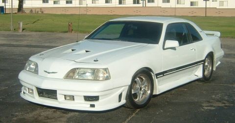 1987 Ford Thunderbird - A white 1987 Ford Thunderbird coupe with a custom body kit and hood scoops is parked outdoors.