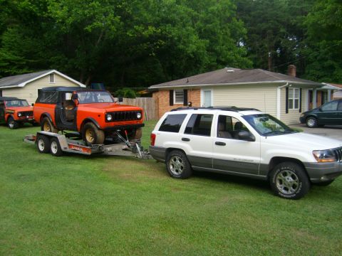 1994 Ford Bronco - A white Jeep Grand Cherokee tows an orange International Scout on a trailer, with another orange vehicle following behind it.