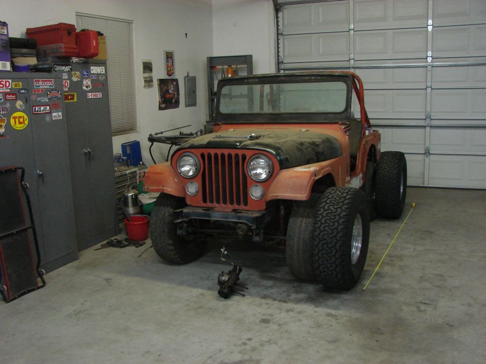Orange Jeep CJ5 with large tires parked in a garage