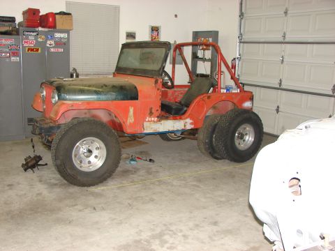 1978 Ford Bronco - This orange Jeep CJ5 is in a garage, appearing to be undergoing some modifications or repairs, with a roll cage and dual rear wheels visibl…