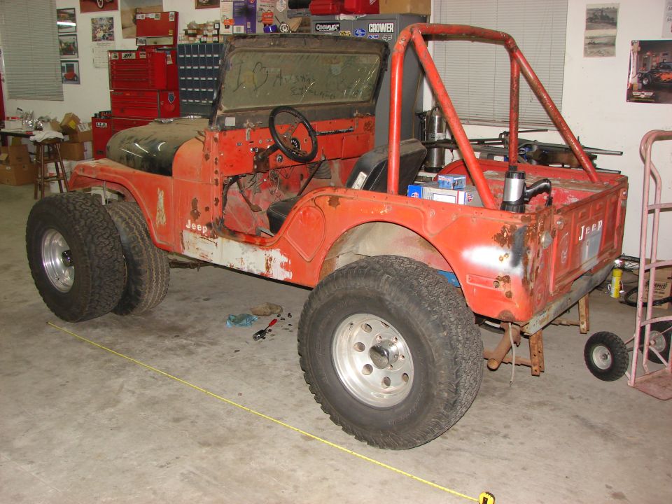 Faded orange Jeep CJ project stripped to bare tub with red roll bar in a shop