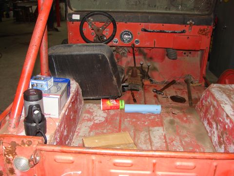 1978 Ford Bronco - The interior of a red Jeep shows a steering wheel, dashboard, and floor with various items scattered around.