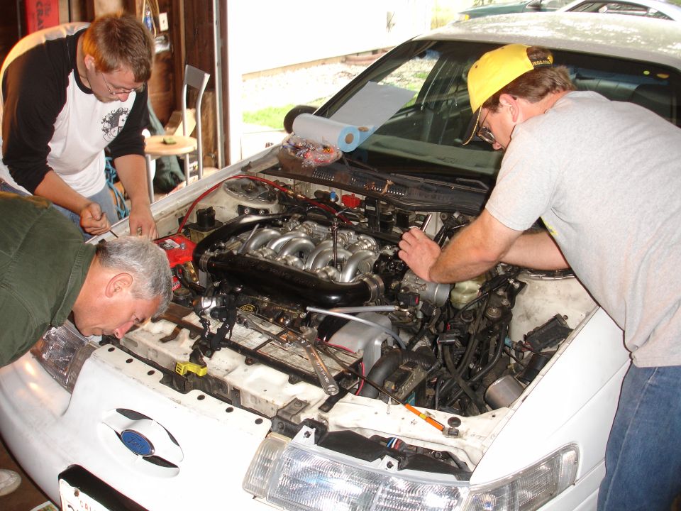White 1993 Ford Taurus engine bay with three men working on the engine