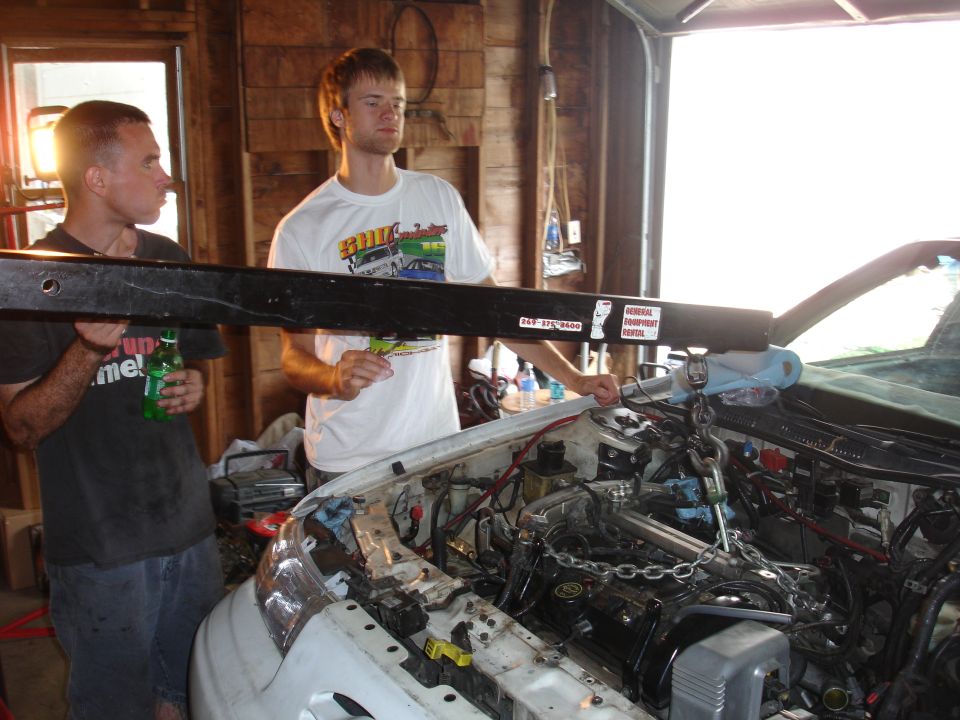 White 1993 Ford Taurus engine bay with engine hoist and two men