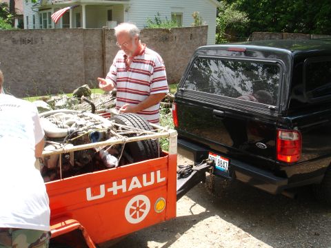 1993 Ford Taurus - A man gestures towards a U-Haul trailer loaded with an engine, hitched to a black Ford pickup truck.