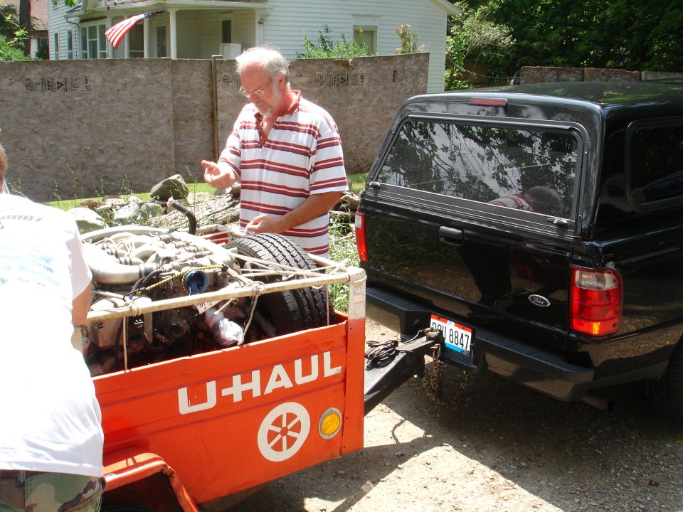 Black Ford pickup truck with a U-Haul trailer carrying an engine