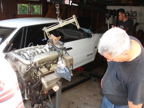 1993 Ford Taurus - A white car's engine is being removed in a garage setting.