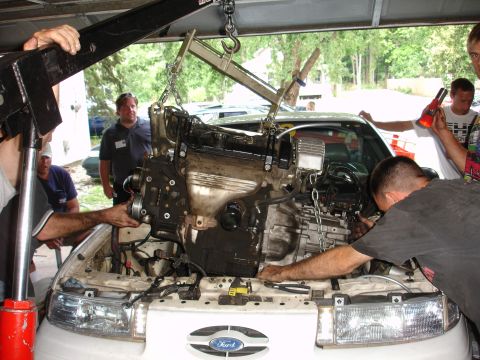 1993 Ford Taurus - Engine removal in progress on a 1993 Ford Taurus, assisted by multiple individuals and an engine hoist.