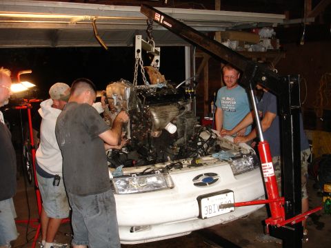 1993 Ford Taurus - Mechanics work on removing an engine from a white car in a garage.