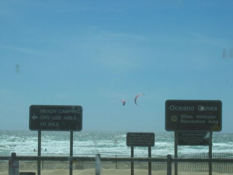 1989 Ford Bronco - Signs indicate Oceano Dunes State Vehicular Recreation Area and beach camping ahead, with kitesurfers visible.