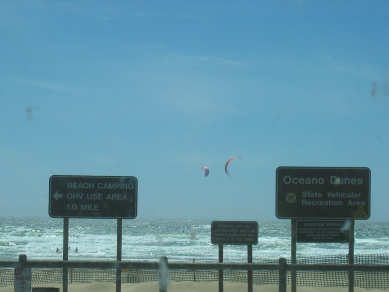 Oceano Dunes State Vehicular Recreation Area sign with beach camping and OHV use area directions; kitesurfers in the distance