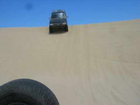 1989 Ford Bronco - A black SUV navigates a steep sand dune on a clear day, with a spare tire visible in the foreground.